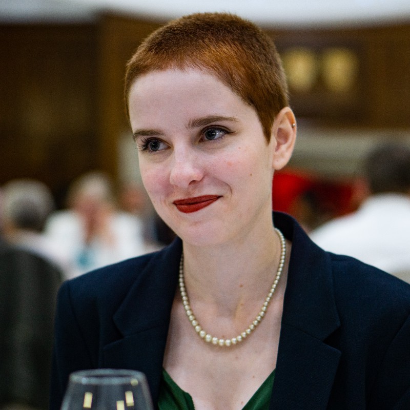 Picture of a woman with short hair, smiling. She is wearing a blue suit jacked and a green blouse.